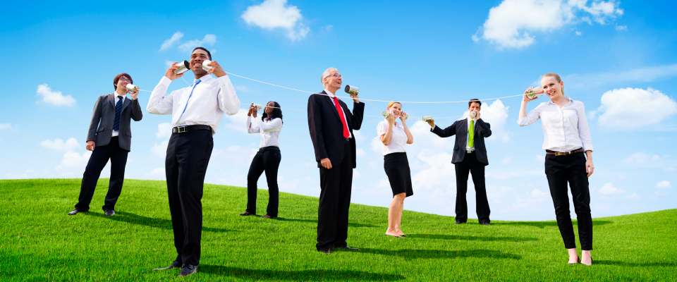 Изображение. Офисные сотрудники в деловой одежде общается с помощью игрушечных приспособлений на фоне зелёного поля и ясного неба