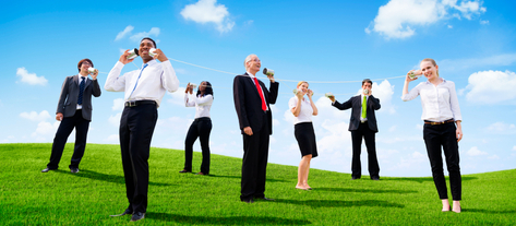 Изображение. Офисные сотрудники в деловой одежде общается с помощью игрушечных приспособлений на фоне зелёного поля и ясного неба